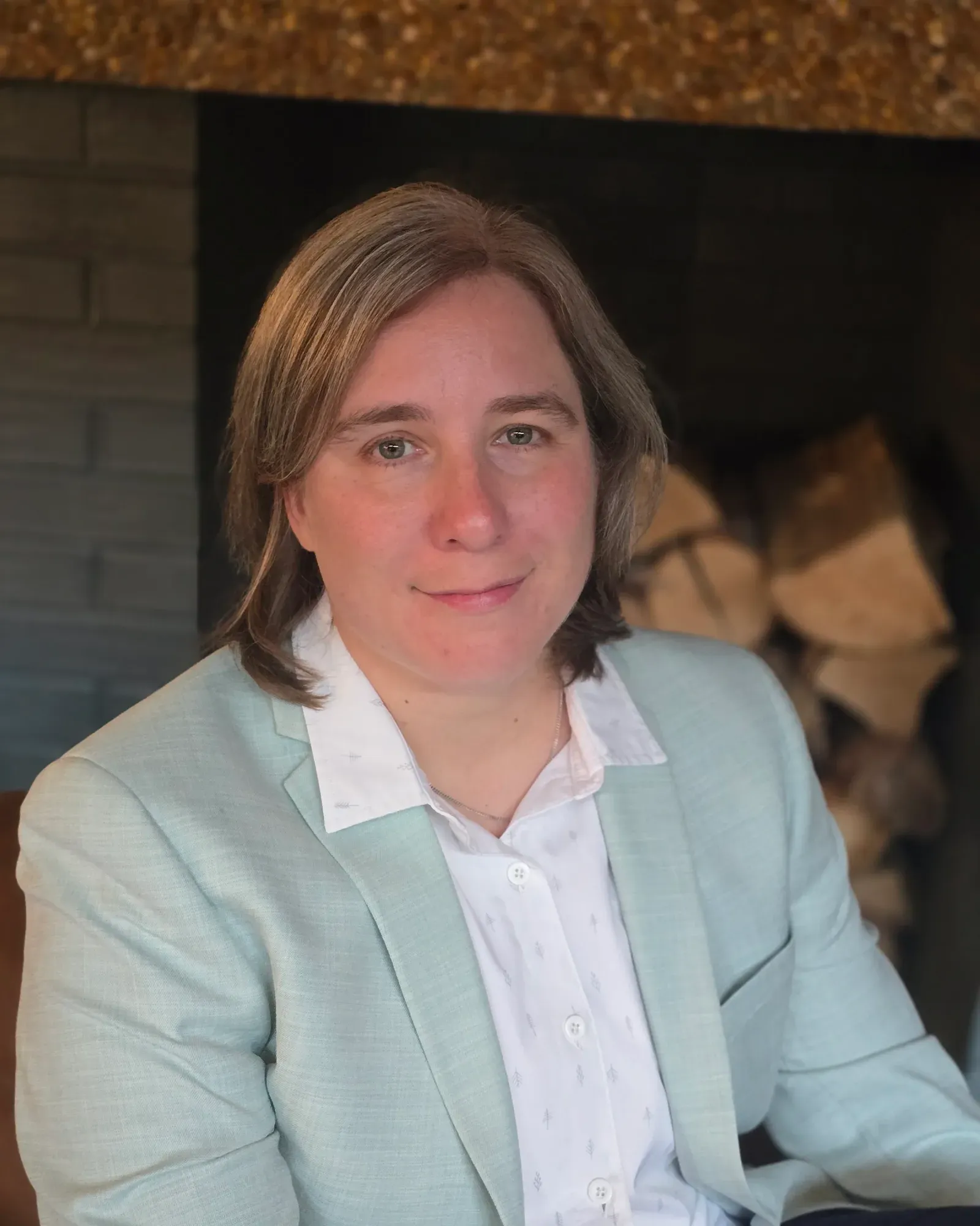 Portrait of Jamie Scrimger, seated indoors in a light green blazer and white shirt, looking at the camera.